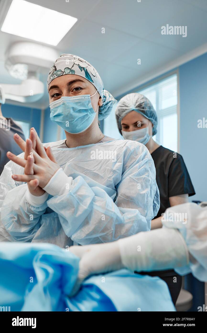 Medizinische Assistentin, die einem Chirurgen hilft, sterile Kleidung anzuziehen Ein Operationssaal Stockfoto
