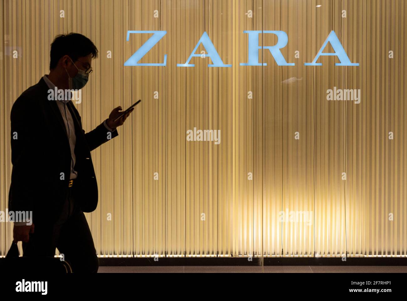 Ein Shopper, der sein Smartphone benutzt, geht am spanischen multinationalen Bekleidungsdesign-Einzelhandelsunternehmen by Inditex, dem Zara-Laden und -Logo in Hongkong vorbei. Stockfoto