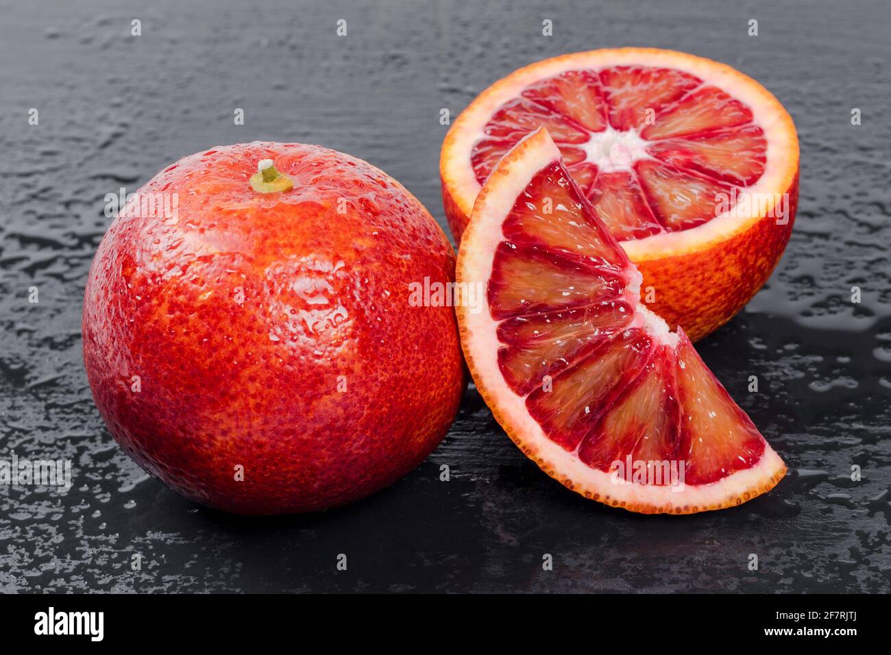 Blutige Orangen ganz und halbiert auf schwarzem Schieferbrett mit Wassertropfen. Rote sizilianische Orangenfrucht Stockfoto