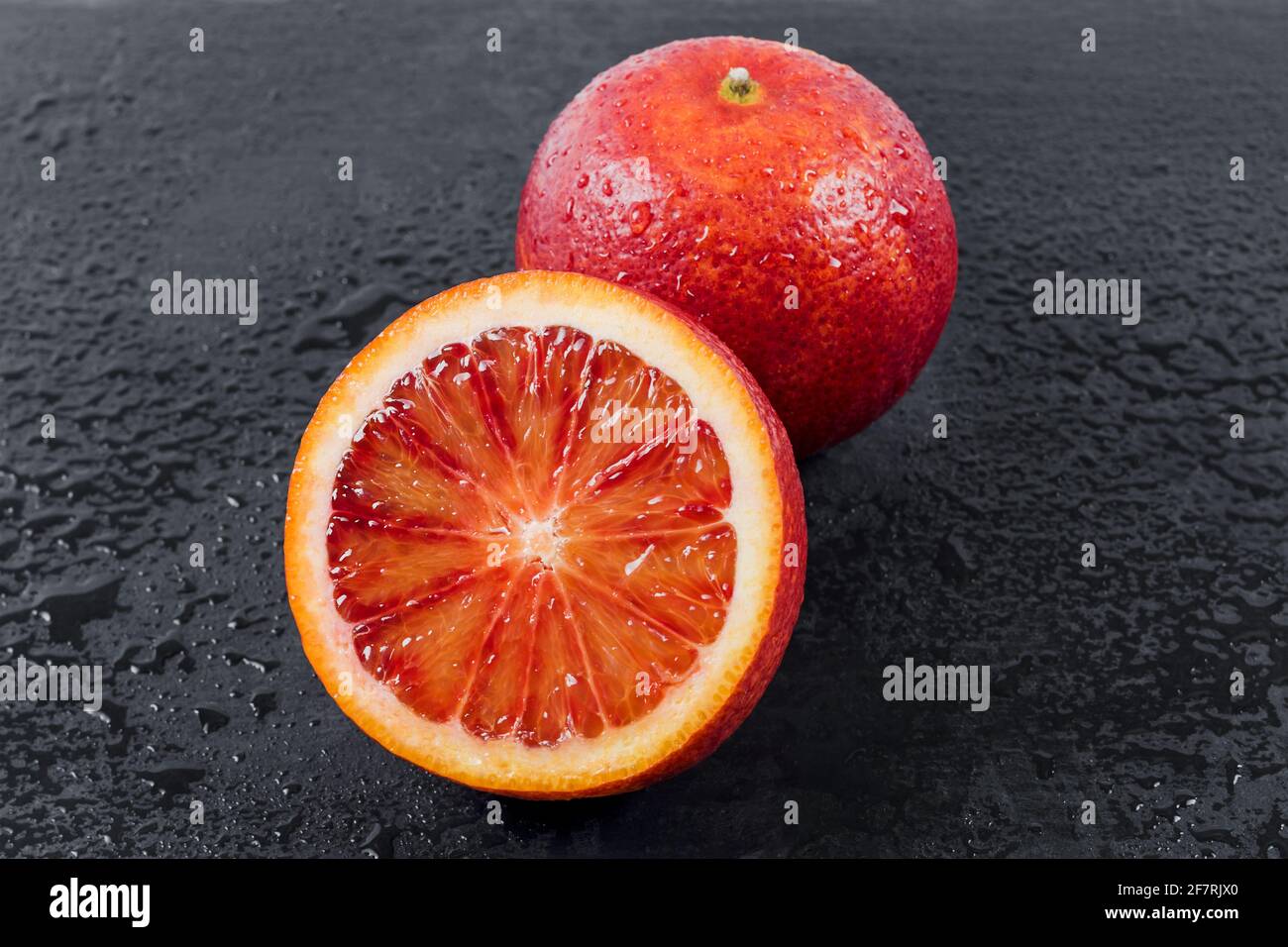 Blutige Orangen ganz und halbiert auf schwarzem Schieferbrett mit Wassertropfen. Rote sizilianische Orangenfrucht Stockfoto