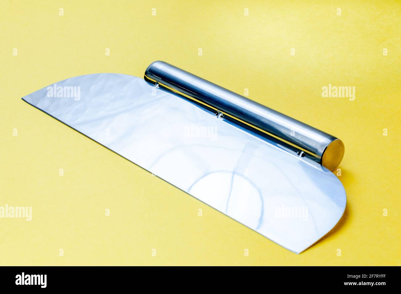 Metall-Teig Schaber Messer über hellgelben Oberfläche Hintergrund. Flacher Teigschaber aus Edelstahl Stockfoto