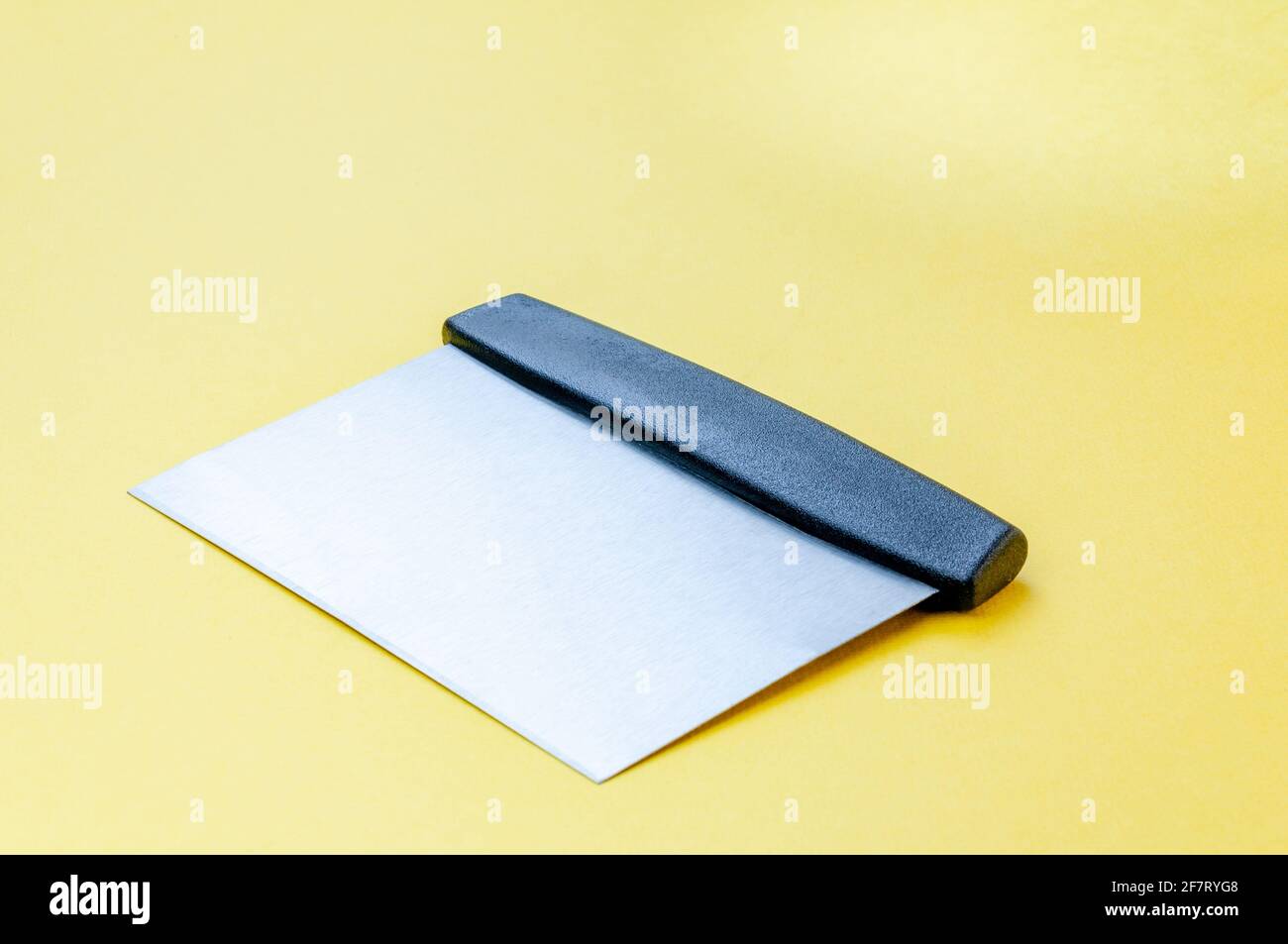 Metall-Teig Schaber Messer über hellgelben Oberfläche Hintergrund. Flacher Teigschaber aus Edelstahl mit Kunststoffgriff Stockfoto