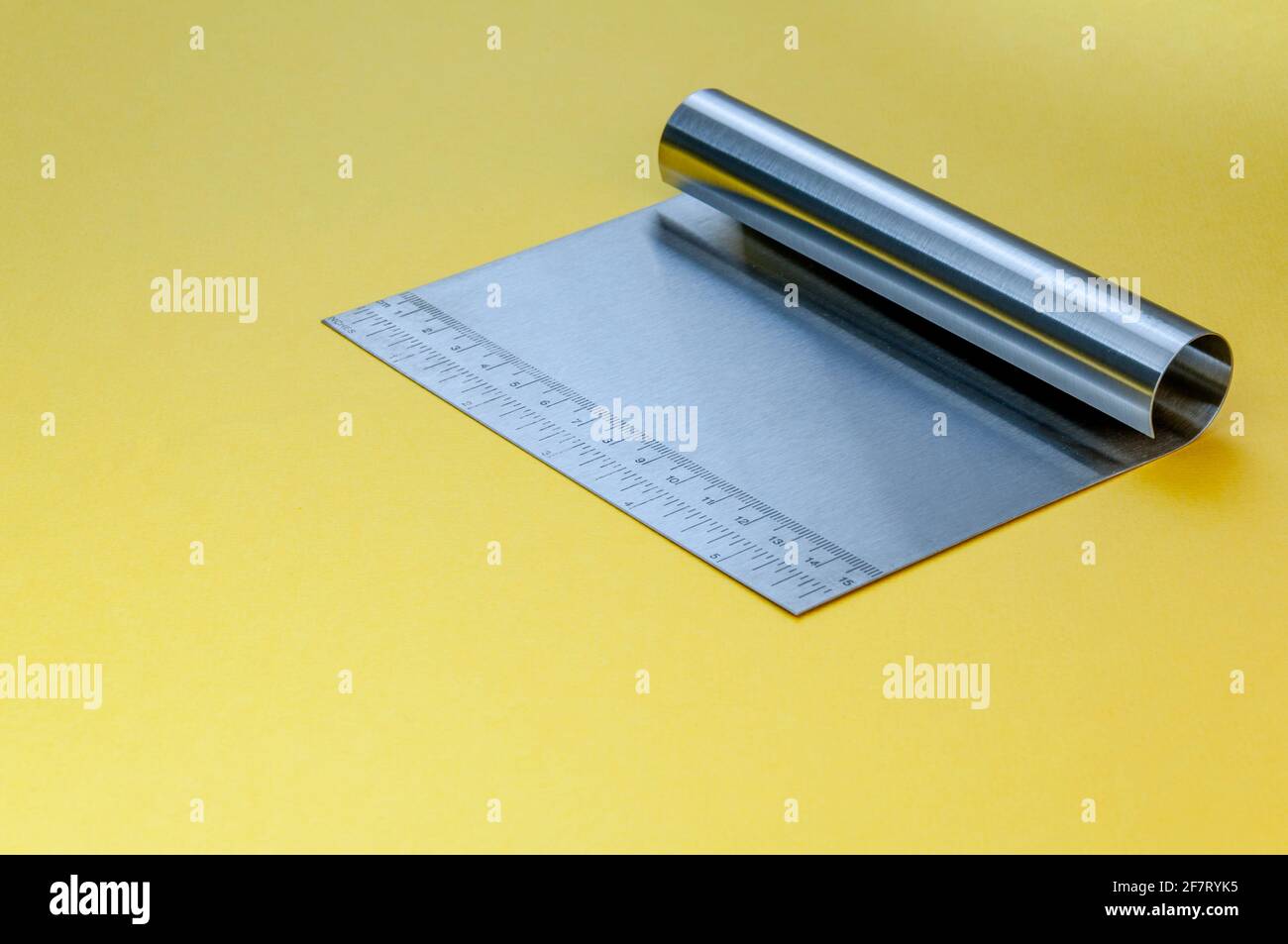 Metall-Teig Schaber Messer über hellgelben Oberfläche Hintergrund. Flacher Teigschaber aus Edelstahl mit Linealskala. Stockfoto