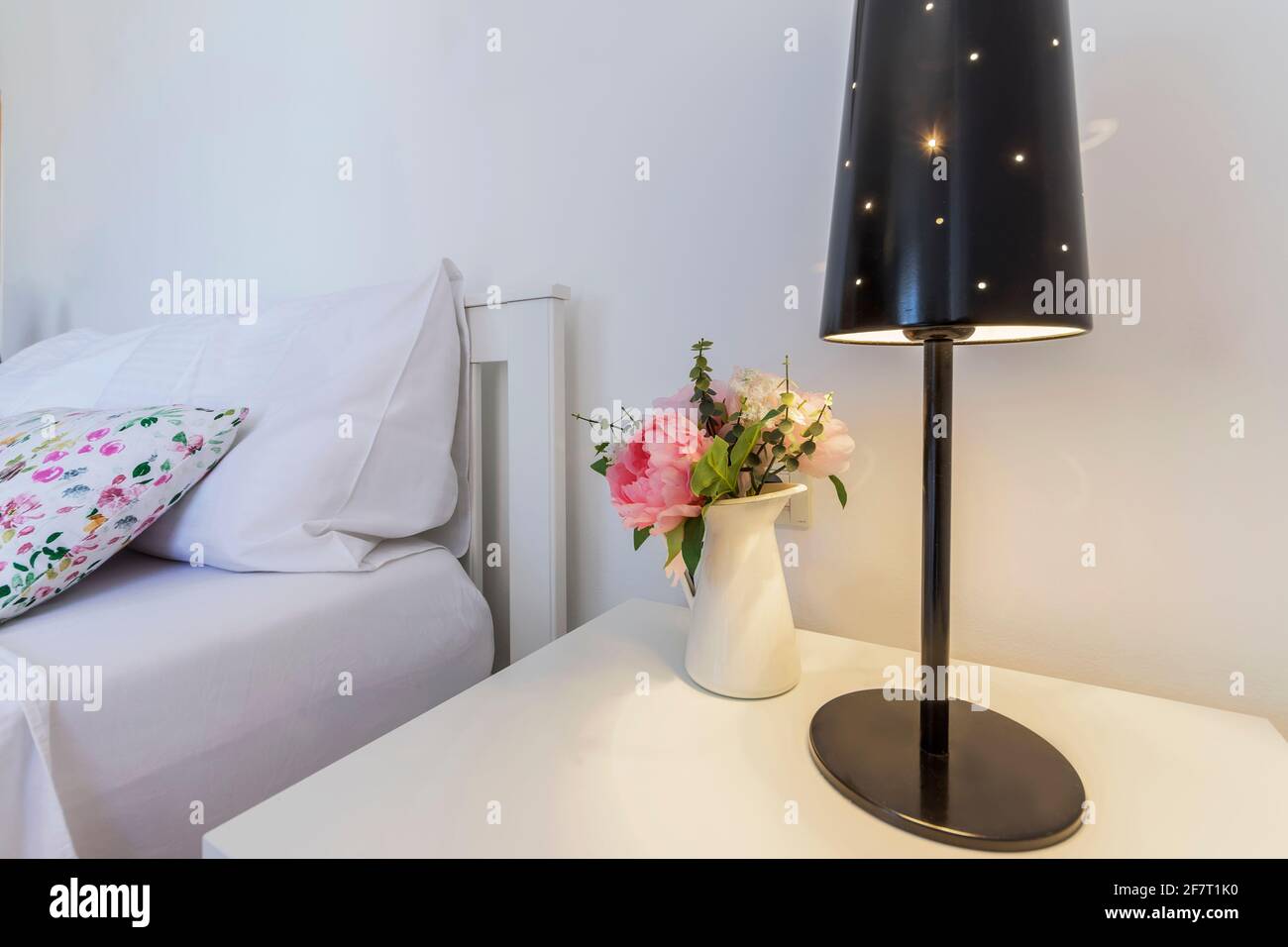 Moderne Schlafzimmerdekoration mit Lampe und Blumen auf Nachttisch Stockfoto