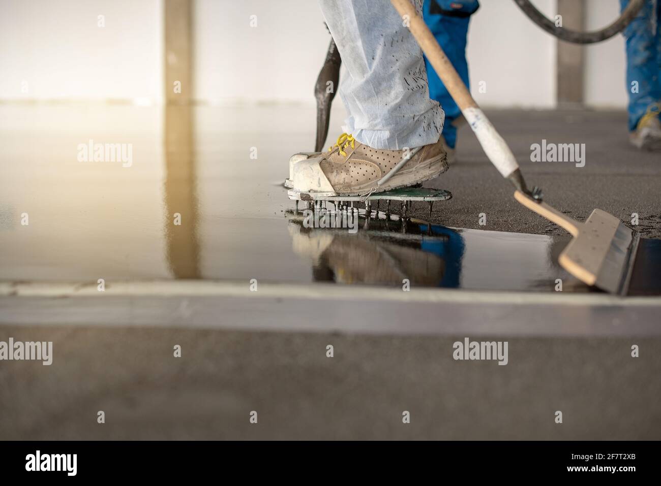 Arbeiter, der auf dem Boden eines Industriegebäudes arbeitet. Bauarbeiter, der Fugen herstellt und nassen Betonboden ausfertigt. Stockfoto