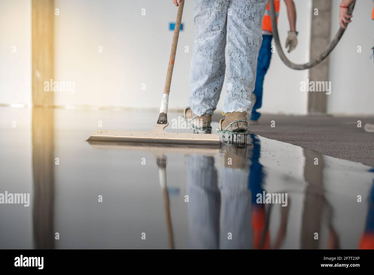 Arbeiter, der auf dem Boden eines Industriegebäudes arbeitet. Bauarbeiter, der Fugen herstellt und nassen Betonboden ausfertigt. Stockfoto
