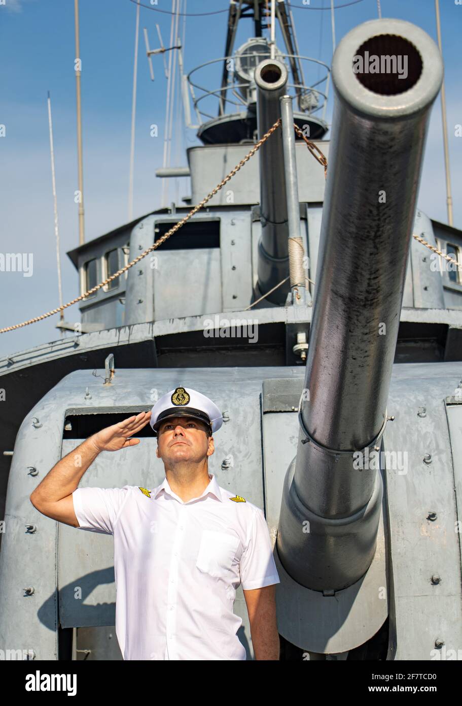 Ein Navy Officer stehen unter der Kanone und würdigen. Der Kapitän in weiße Uniform steht an Bord eines Schiffes und salutierte. Stockfoto