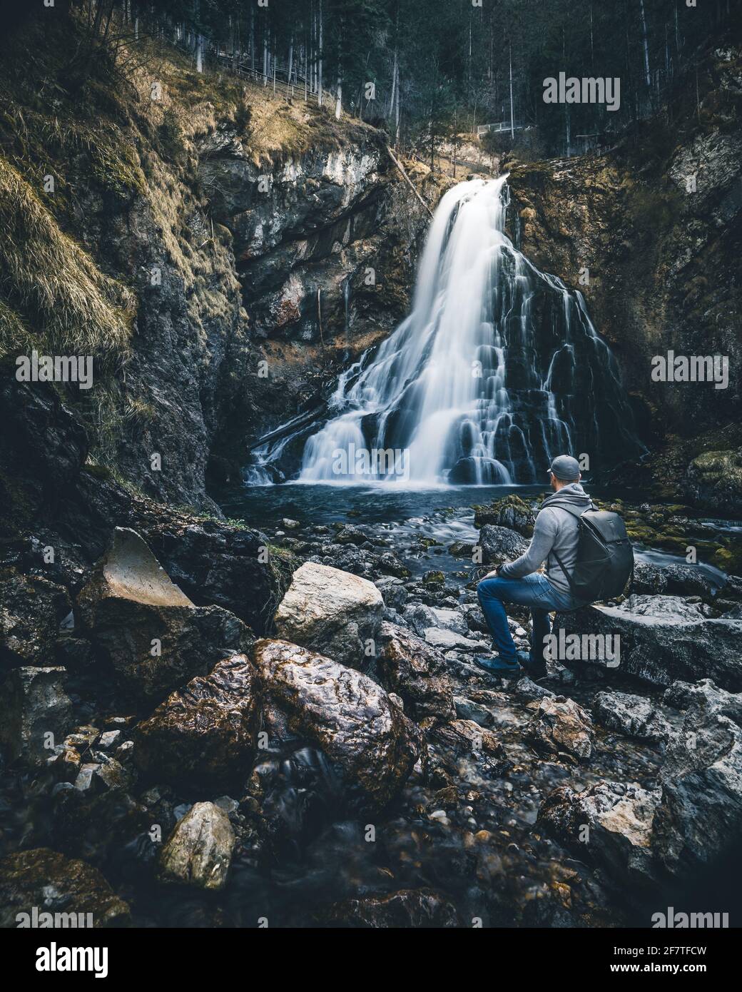 Mann mit Rucksack sitzt vor dem Wasserfall Stockfoto