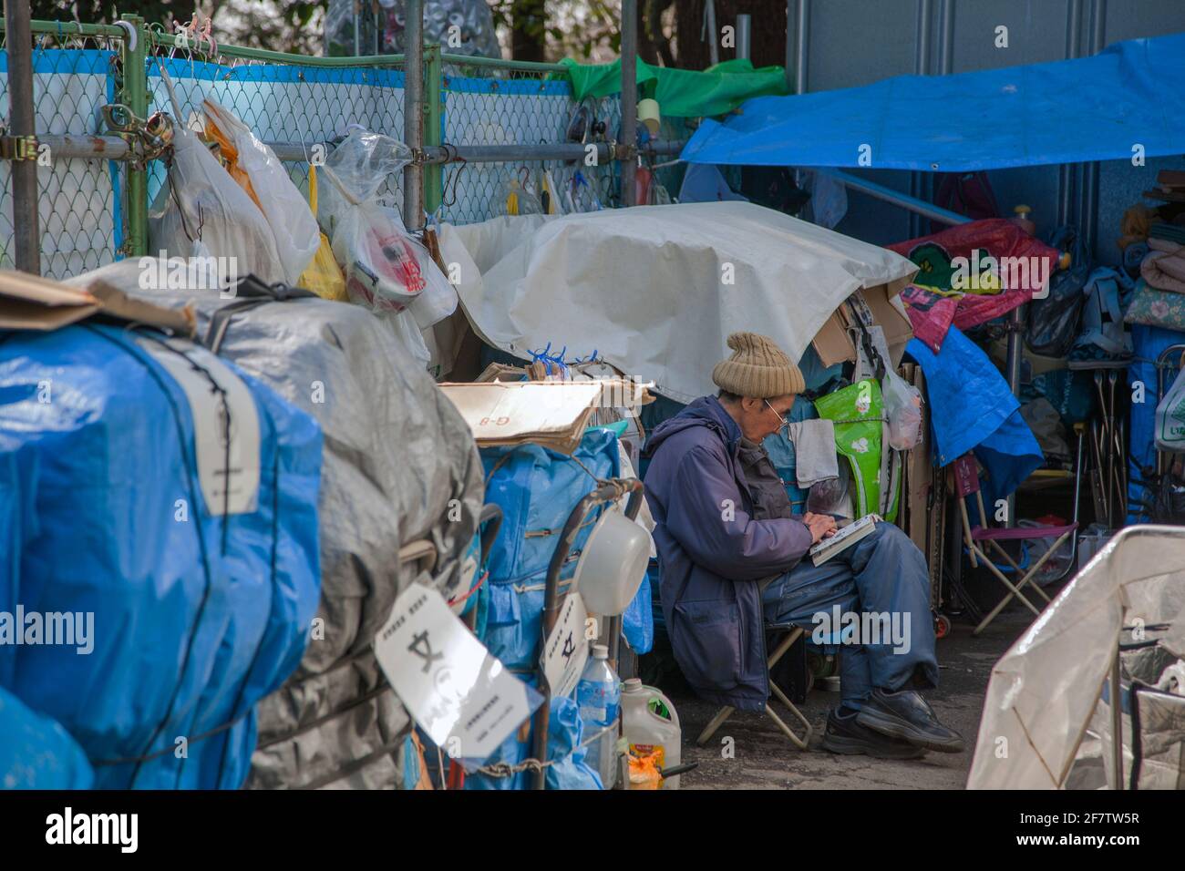 Japanischer Obdachloser sitzt in der Gegend, in der er seinen Besitz im Ueno Park, Tokio, Japan, beherbergt, beim Lesen von Manga-Comics Stockfoto