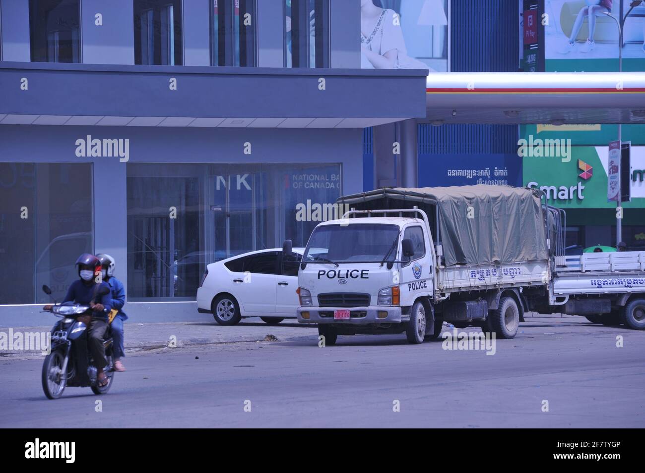 Aufgrund eines kürzlichen Ausbruchs von COVID - 19 in einer Bekleidungsfabrik hat die kambodschanische Regierung eine Sperre auferlegt, bei der Motorradfahrer in Schutzmaske an einem Polizeifahrzeug vorbeifahren, das während der Coronavirus-Pandemie zum Aufstellen eines Kontrollpunkts verwendet wird. Stueng Meanchey, Phnom Penh, Kambodscha. April 2021. © Kraig Lieb Stockfoto