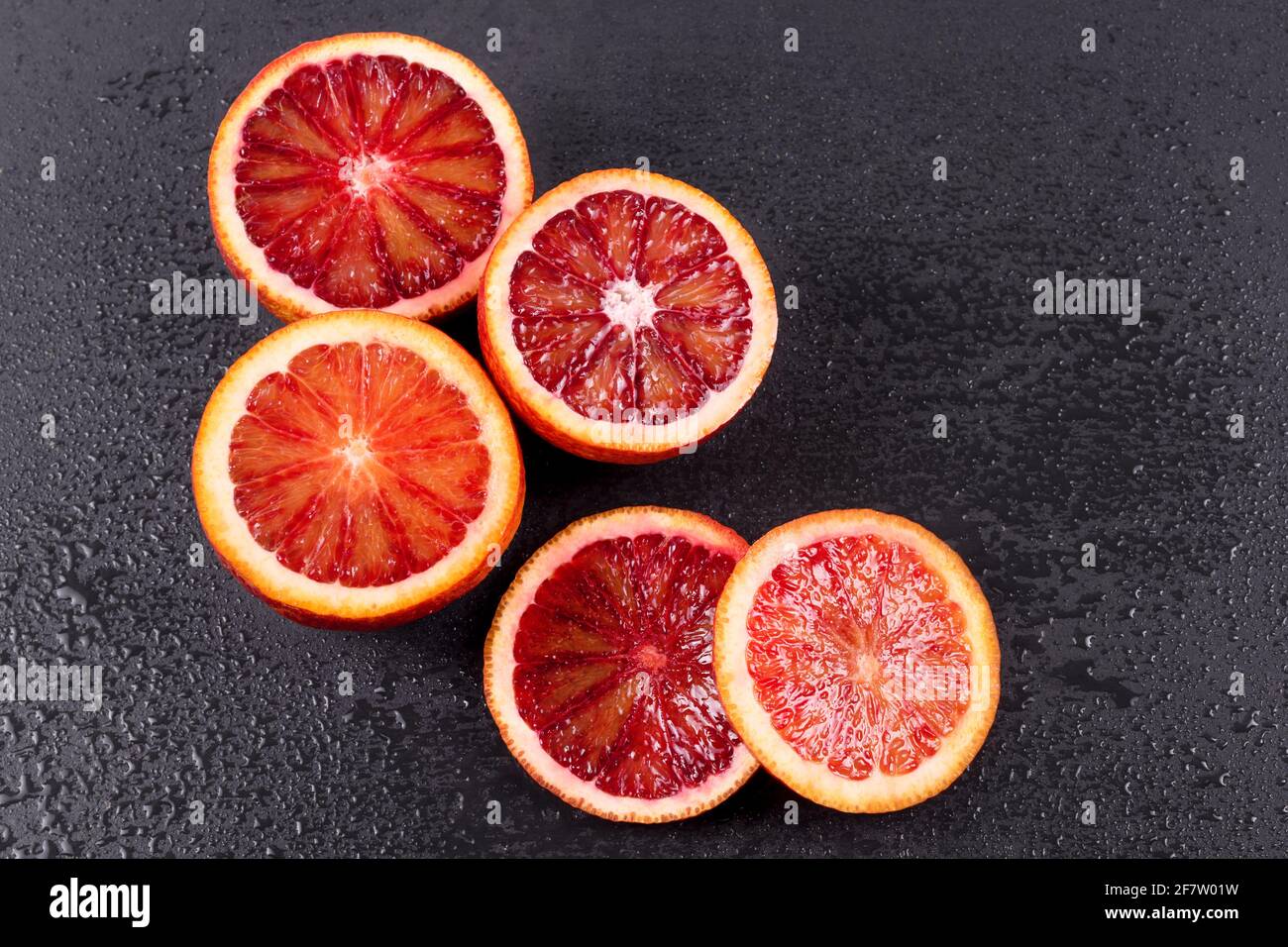 Blutige Orangen in zwei Hälften geschnitten und auf schwarzem Schieferbrett mit Wassertropfen geschnitten. Rote sizilianische Orangenfrucht. Draufsicht, freier Platz für Text. Stockfoto