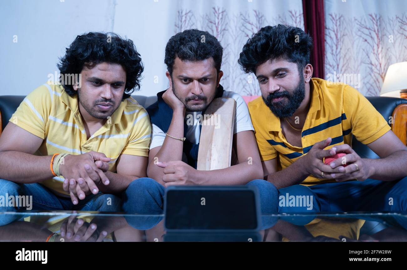 Drei indische junge Cricket-Fans halten Fledermaus und Ball beobachten interessante Live-Streaming-Cricket-Spiel auf dem Handy von zu Hause aus. Stockfoto