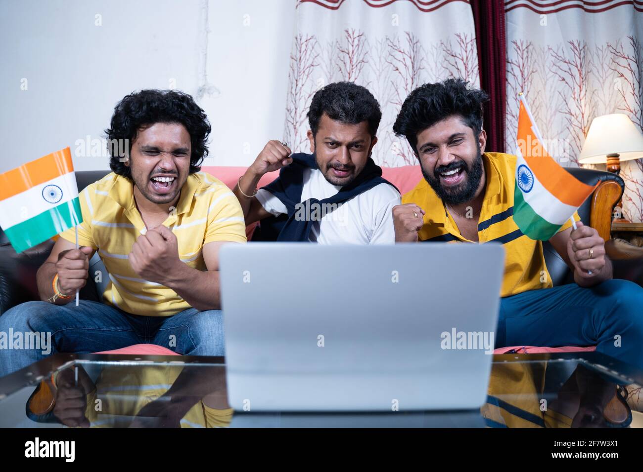 Drei junge Menschen unterstützen das indische Team, indem sie indische Flaggen halten Beim Live-Streaming von Cricket-Spielen auf dem Laptop Stockfoto