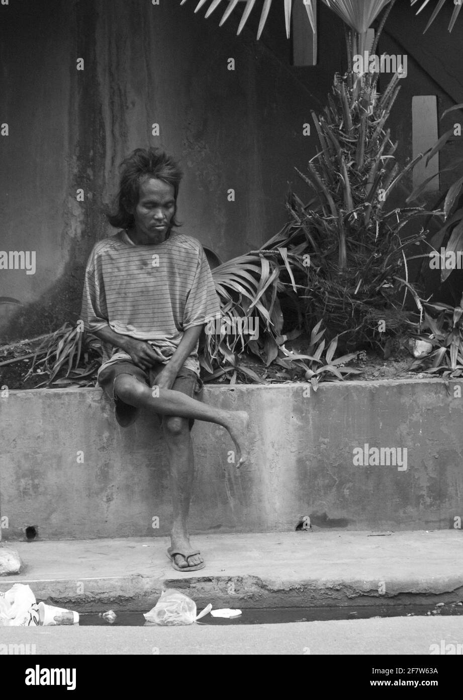 CEBU, PHILIPPINEN - 19. Jan 2009: Ein Straßenbewohner sitzt auf einem Blumentopf entlang einer belebten Straße in Cebu Stockfoto
