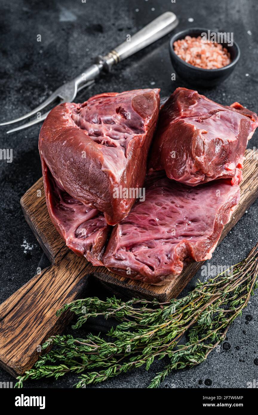 Rohes geschnittes Rind- oder Kalbsherz auf einem Schlachtbrett. Schwarzer Hintergrund. Draufsicht Stockfoto