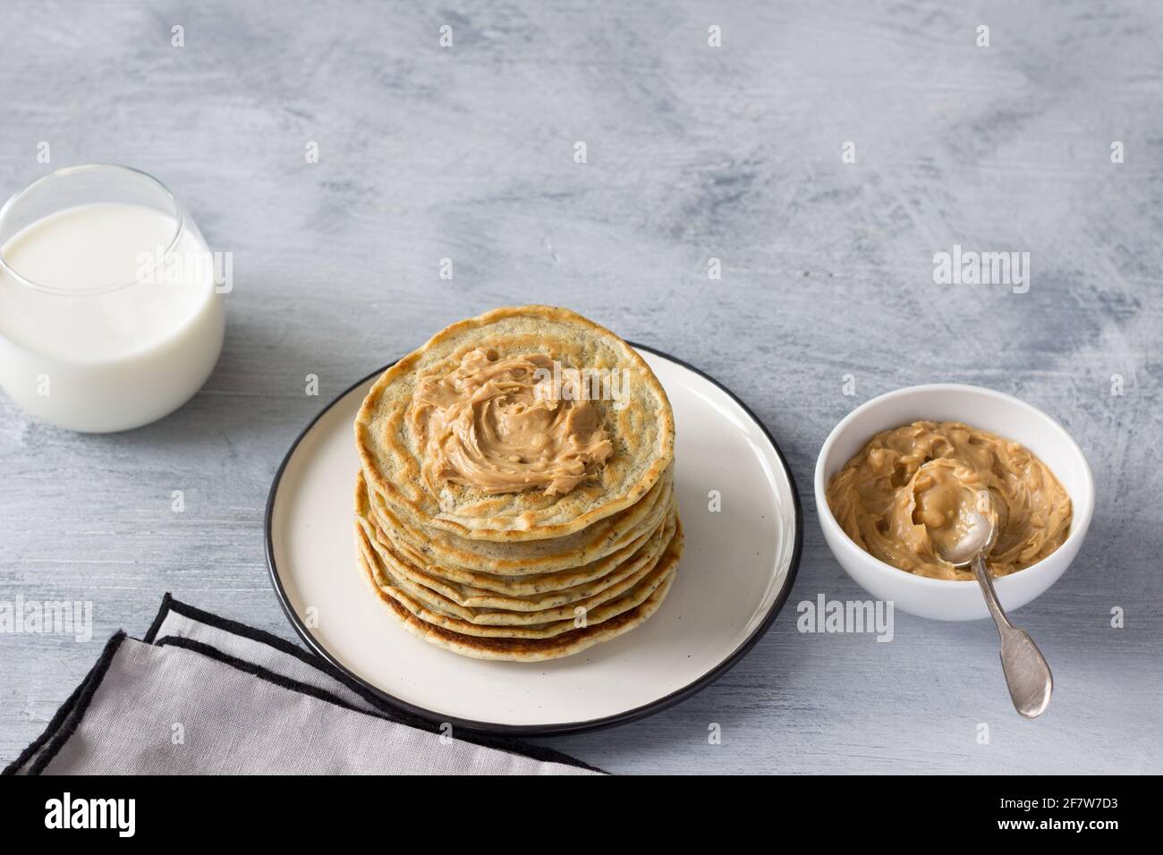Vegane Pfannkuchen mit Leinsamen, Erdnussbutter und veganer Milch auf einem weißen Teller auf grauem Hintergrund. Leckere hausgemachte gesunde Speisen Stockfoto
