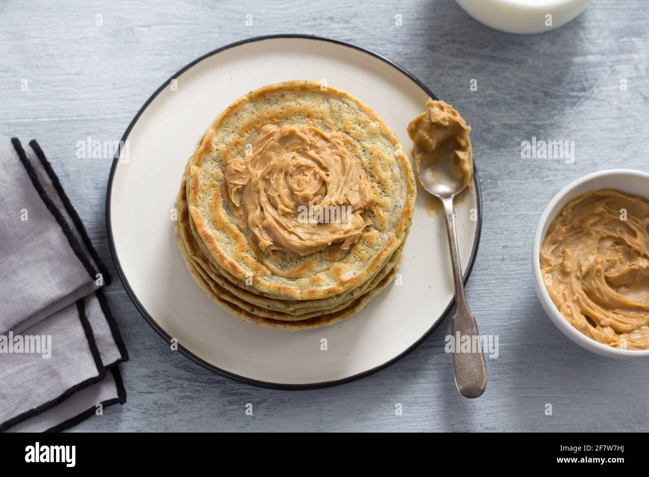 Vegane Pfannkuchen mit Leinsamen, Erdnussbutter und veganer Milch auf einem weißen Teller auf grauem Hintergrund. Leckere hausgemachte gesunde Speisen Stockfoto
