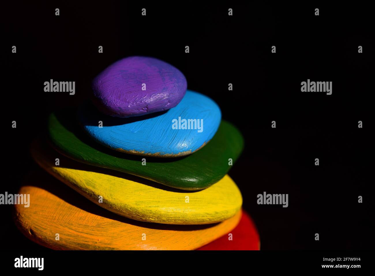 Mehrere bunte Kieselsteine, die in Regenbogenfarben gemalt sind, liegen darauf Übereinander vor einem dunklen Hintergrund Stockfoto