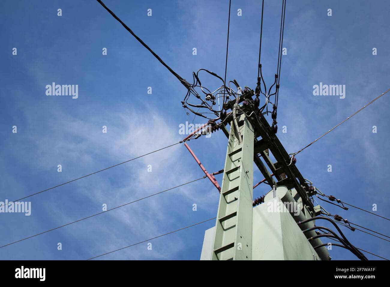 Ein Mast mit einem Netzwerk aus vielen verschiedenen Stromkabeln Wird von unten gegen den blauen Himmel mit Wolken fotografiert Stockfoto