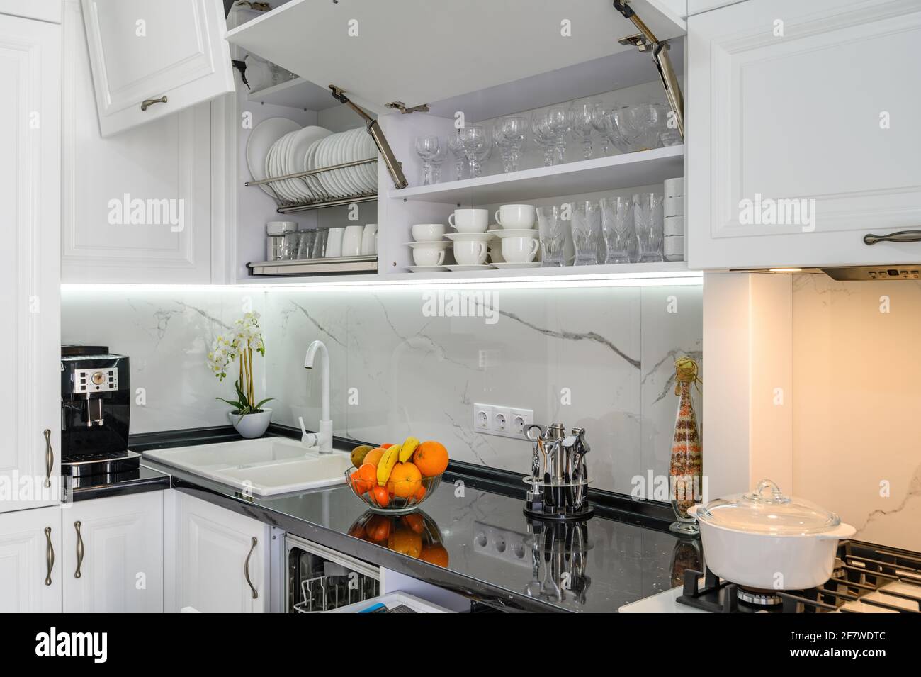 Luxuriöse weiße moderne Kücheneinrichtung, Schubladen herausgezogen, Türen offen Stockfoto