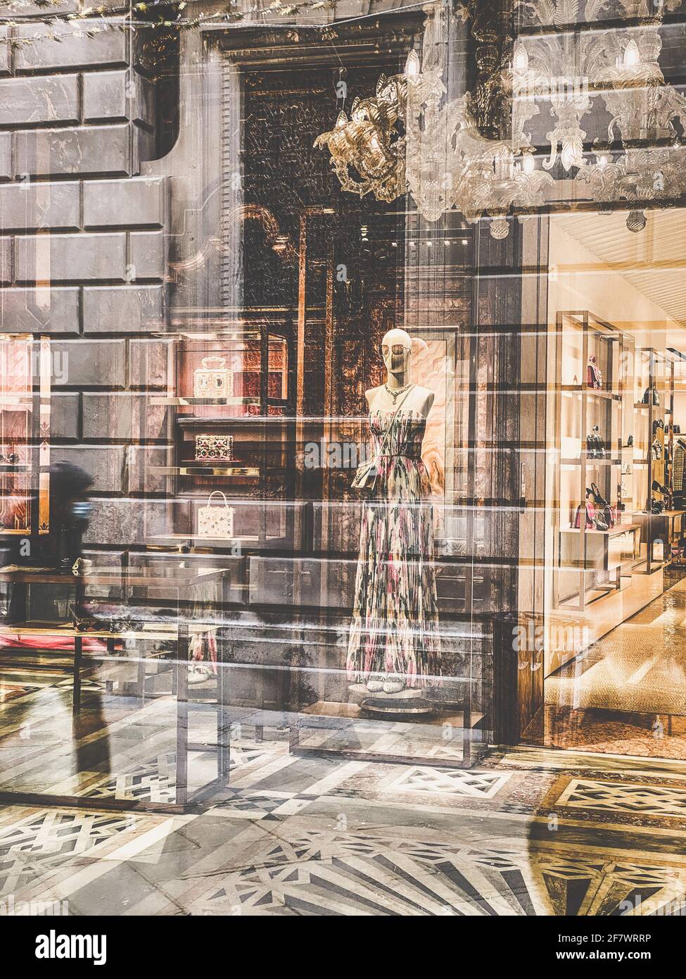 Spiegelung einer Person, die vor dem Fenster eines großen Modehauses läuft, das wegen des Covid-19 geschlossen wurde. Durch das Fenster können wir ein Mannequin sehen Stockfoto