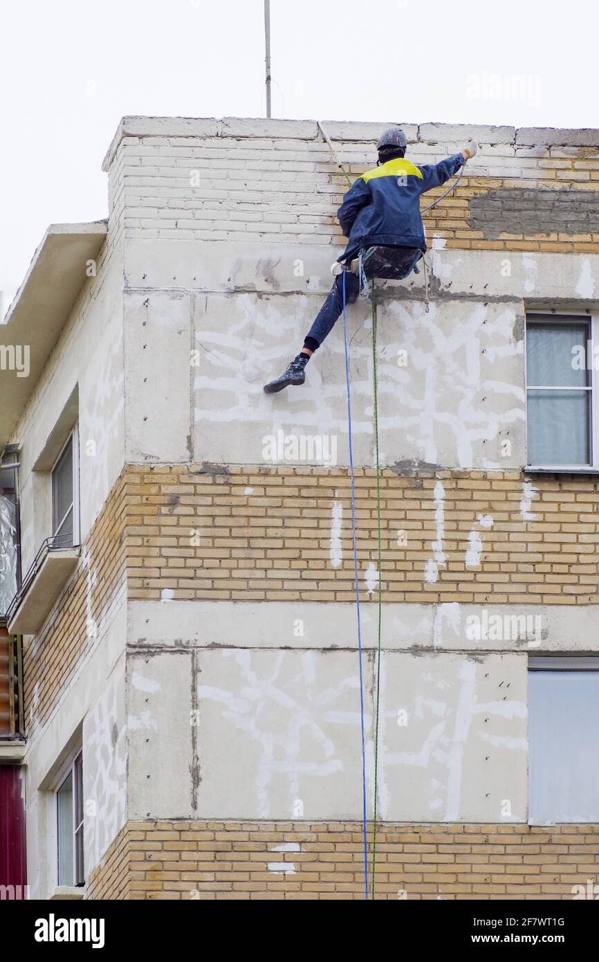 Ein Gipser an der Wand eines Hauses arbeitet mit Kletterausrüstung. Industriekletterer schließen Risse in der Wand eines alten mehrstöckigen Gebäudes Stockfoto