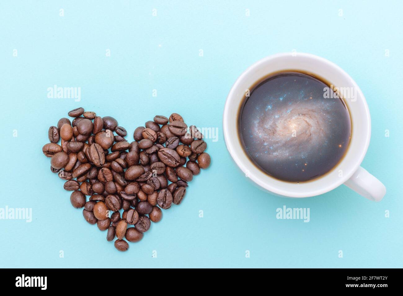 Tasse schwarzen Kaffee mit Schaumstoff in Form einer Galaxie, Kaffeekörner in Form eines Herzens auf blauem Hintergrund, Draufsicht. Kaffee am Morgen für geliebt Stockfoto