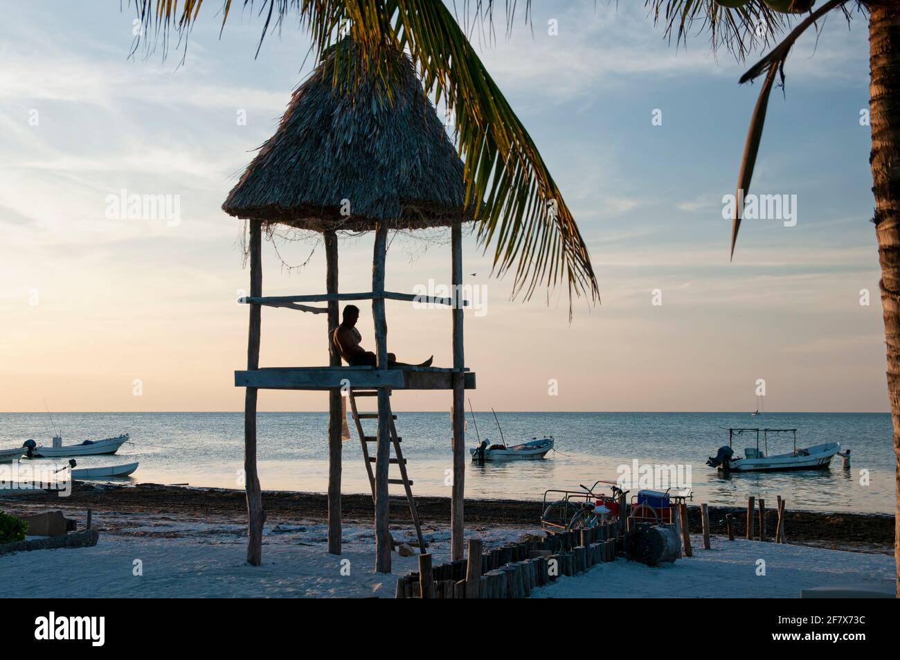 Ein junger Mann über einer rustikalen Hütte am tropischen Strand von Holbox Island in Mexiko blickt über den Horizont des Karibischen Ozeans. Urlaubsreisekonzept. Stockfoto