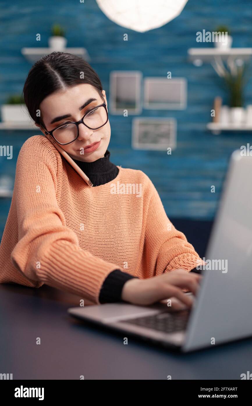 Studenten, die Informationen auf einem Laptop für ein digitales Seminar durchsuchen. Eine Teenager-Frau, die am Telefon telefoniert und Kollegen über Online-Hochschulmeeting informiert, während sie am Schreibtisch im Wohnzimmer sitzt Stockfoto