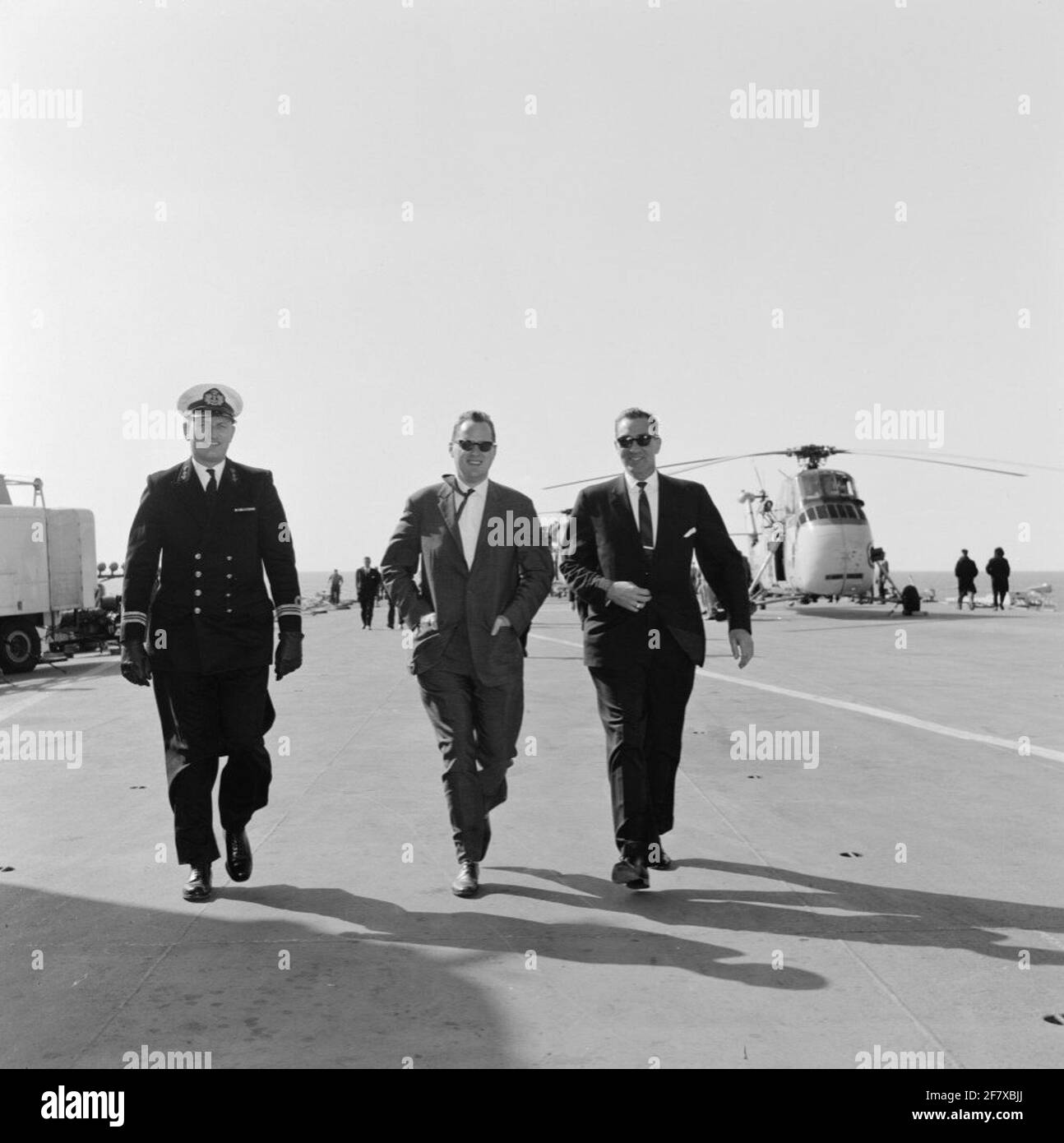 Am 19. September wird das Marijnen-Kabinett (1963-1965) mit dem Flugzeuglager hr.ms segeln. Karel Doorman (R 81) Van Den Helder nach Rotterdam. Einige der Gäste wandern unter der Leitung eines Leutnant-Ter-Meeres der 1. Klasse ​​the (LTZ 1) über das Eseldeck mit einem Transport-/Detektions- und Rettungshubschrauber vom Typ Sikorsky UH-34J im Hintergrund. Stockfoto