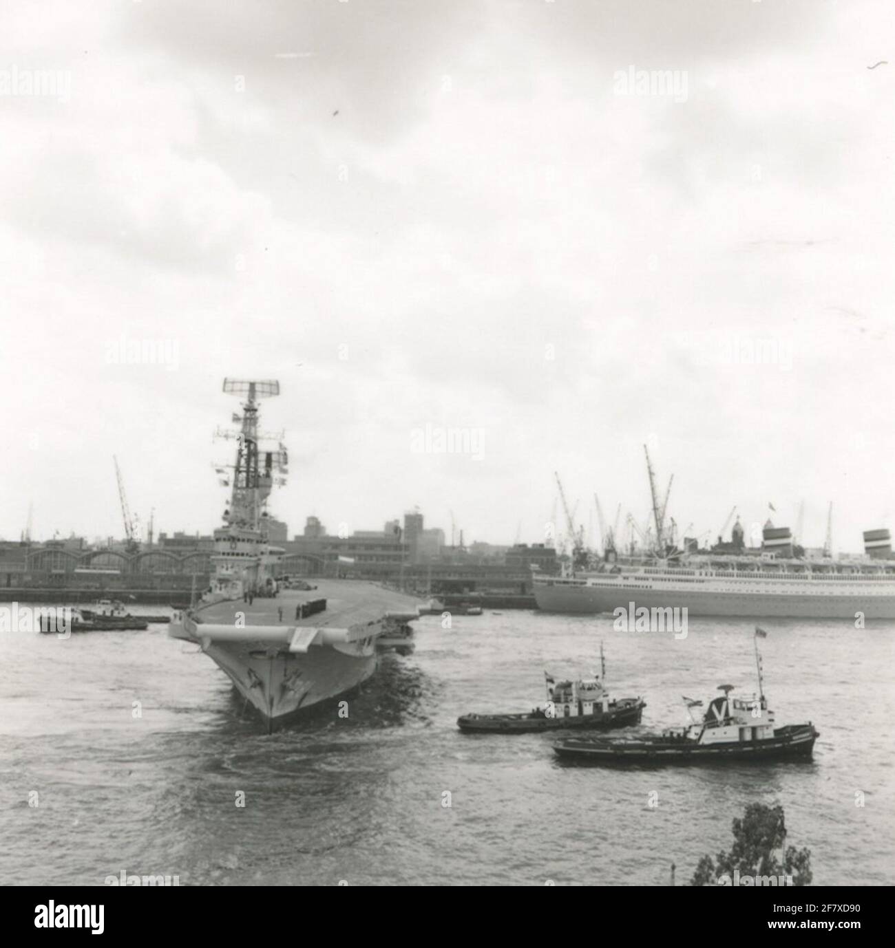 HF.ms. Karel Doorman (1948-1968) wird mit Hilfe von vier Schleppern an den Bäumen festgemacht. Rechts das Passagierschiff Nieuw Amsterdam (1938-1974) der NV Dutch-American Steamvaart Maatschappij Holland-America Line (HAL). Stockfoto