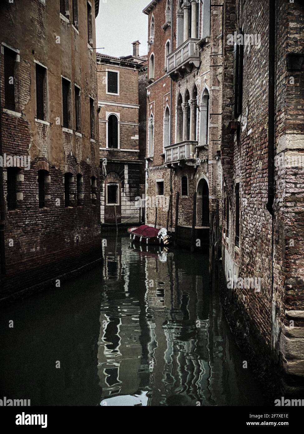 Dunkles Bild, am Abend, eines Bootes in einem kleinen Kanal, im Wasser in Venedig, Italien Stockfoto