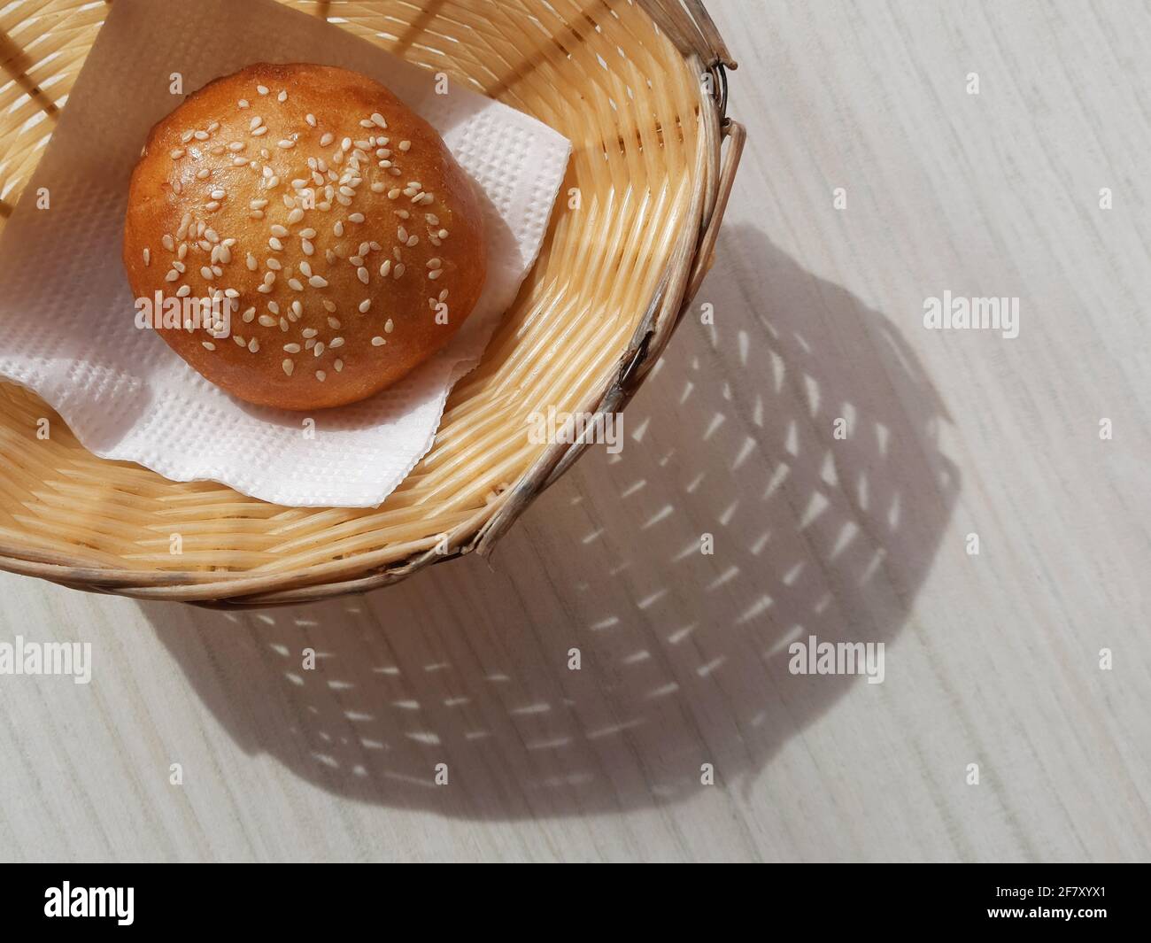 Sonniger Brotkorb mit langem Schatten auf weißem Holztisch von oben. Closeup Bun im Korb modernes Banner Snack Food Deko-Design mit Kopierfläche Stockfoto