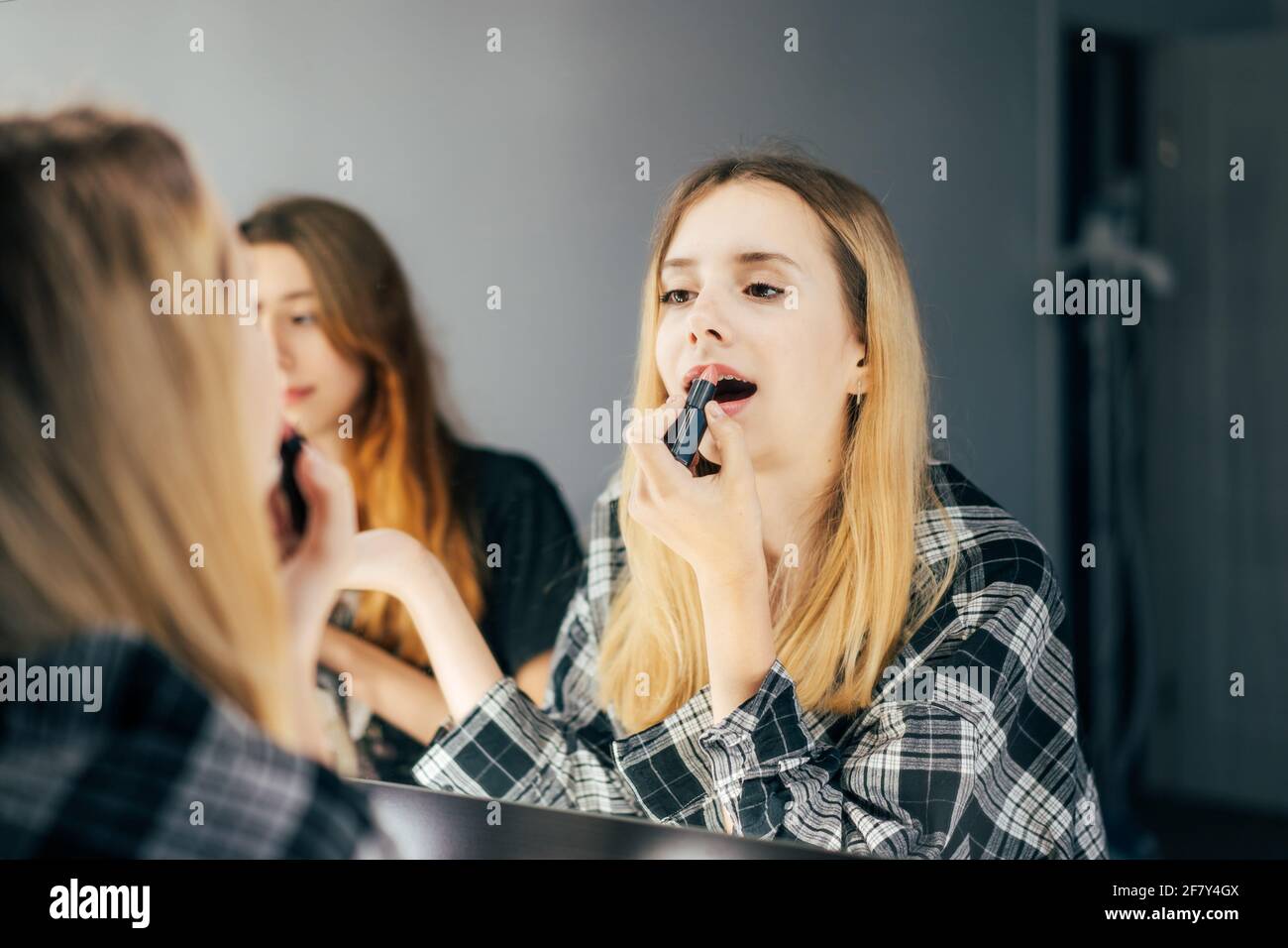 Ein fünfzehnjähriges Teenager-Mädchen schminkten ihre Lippen mit Lippenstift, während sie in einem großen Spiegel in der Garderobe aussiegen. Person vor der Party. Schönheit Stockfoto