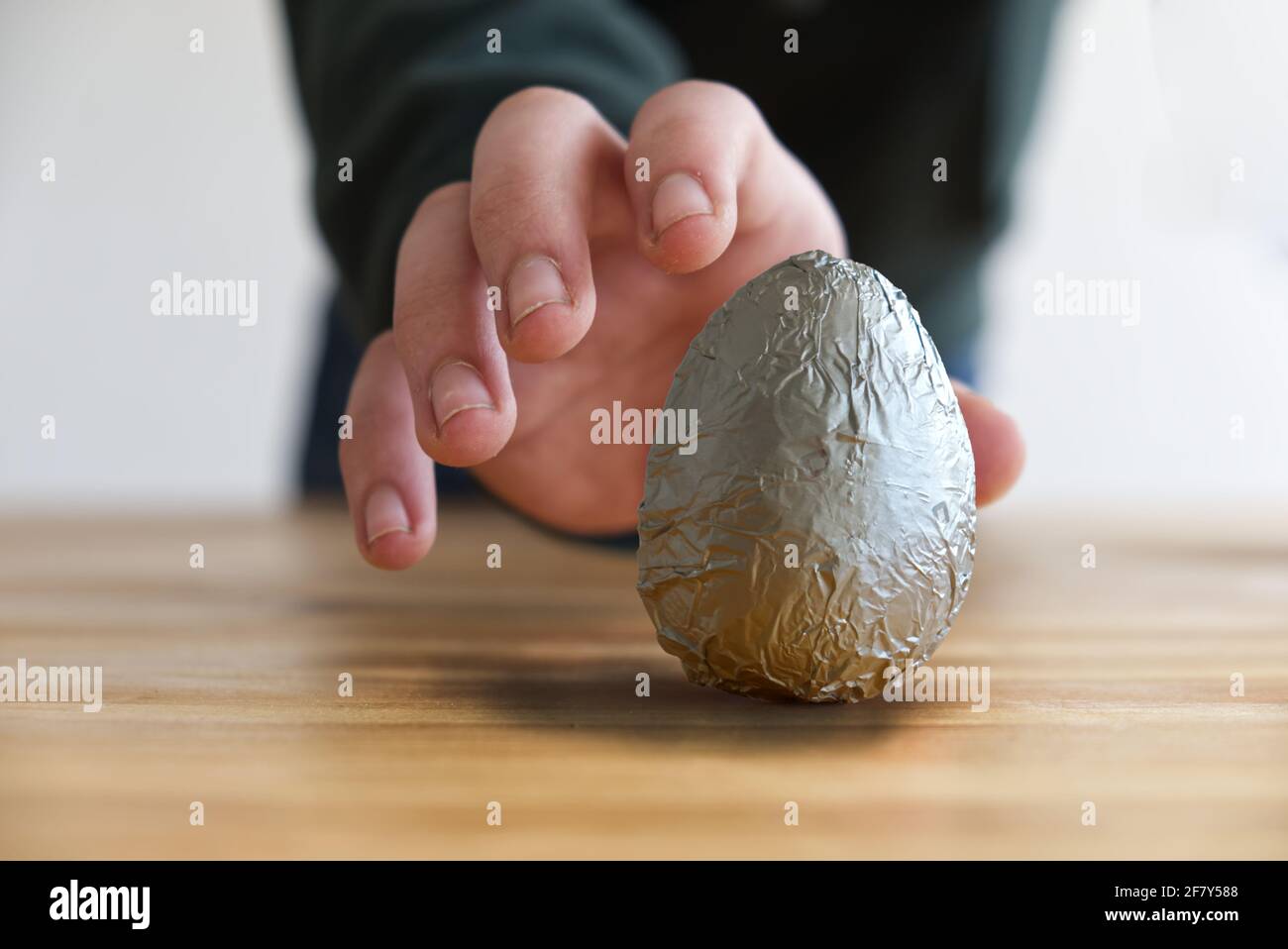 Fotokonzept der Hand eines Kindes, das ein Schokoladenei nimmt Aus dem Tisch Stockfoto