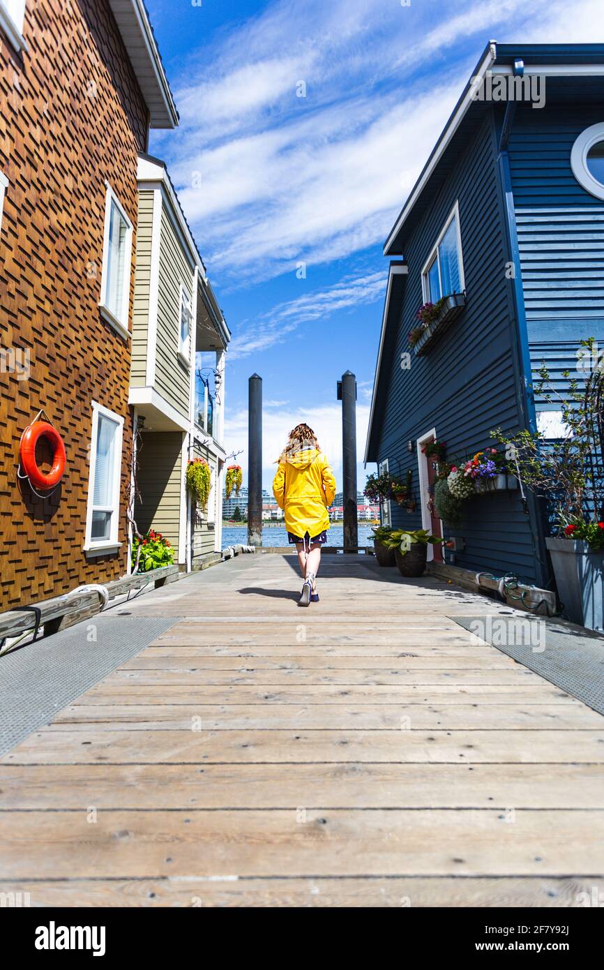 Kaukasisches Mädchen, das im Sommer auf einem hölzernen Fußgängerdock steht Mit hellem Sonnenlicht und schwebenden Häusern an der Seite Stockfoto