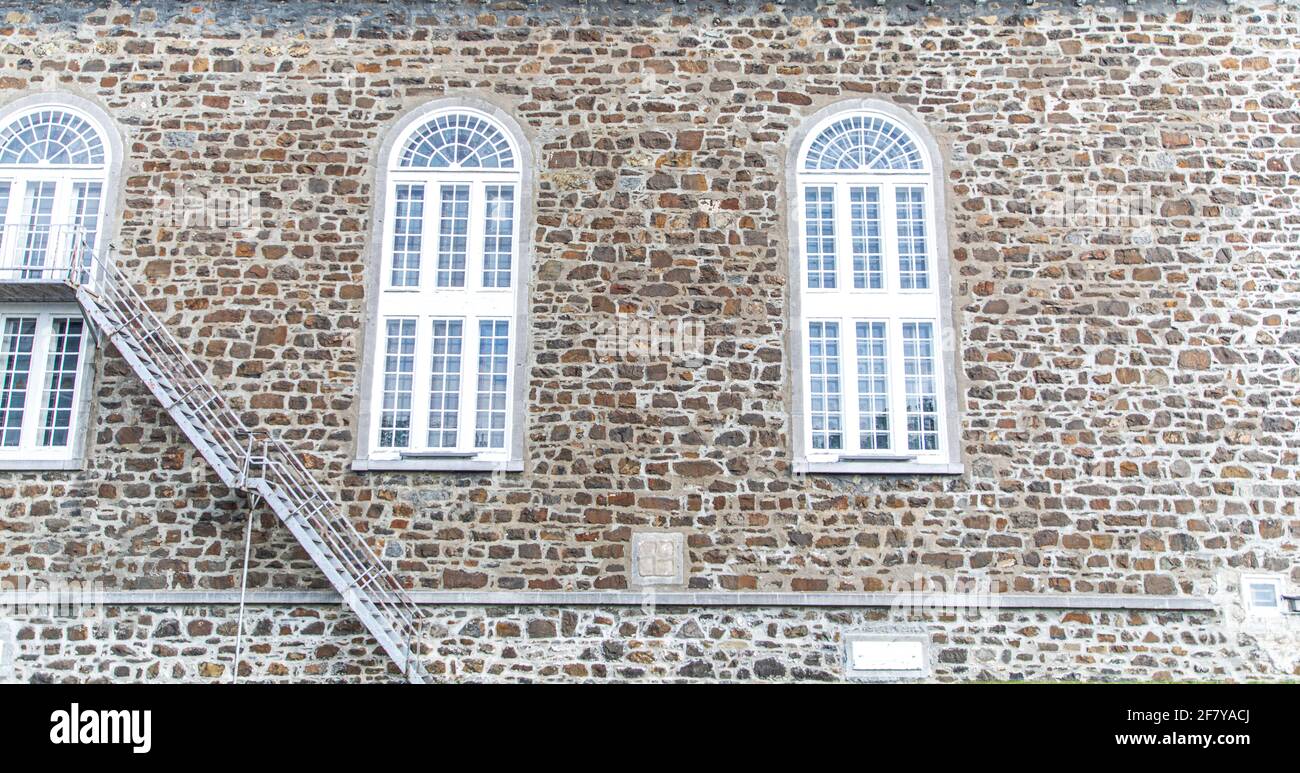 Steinmauer mit hohen Fenstern und Metalltreppen Stockfoto