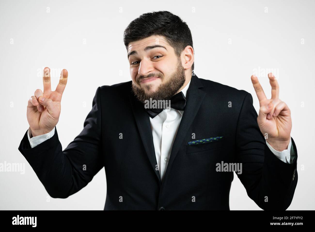 Schöner Mann zeigt mit Händen und zwei Fingern Luft Zitate Geste, biegen Finger isoliert auf weißem Hintergrund. Kerl in schwarzem Smoking. Nicht lustig, Ironie Stockfoto