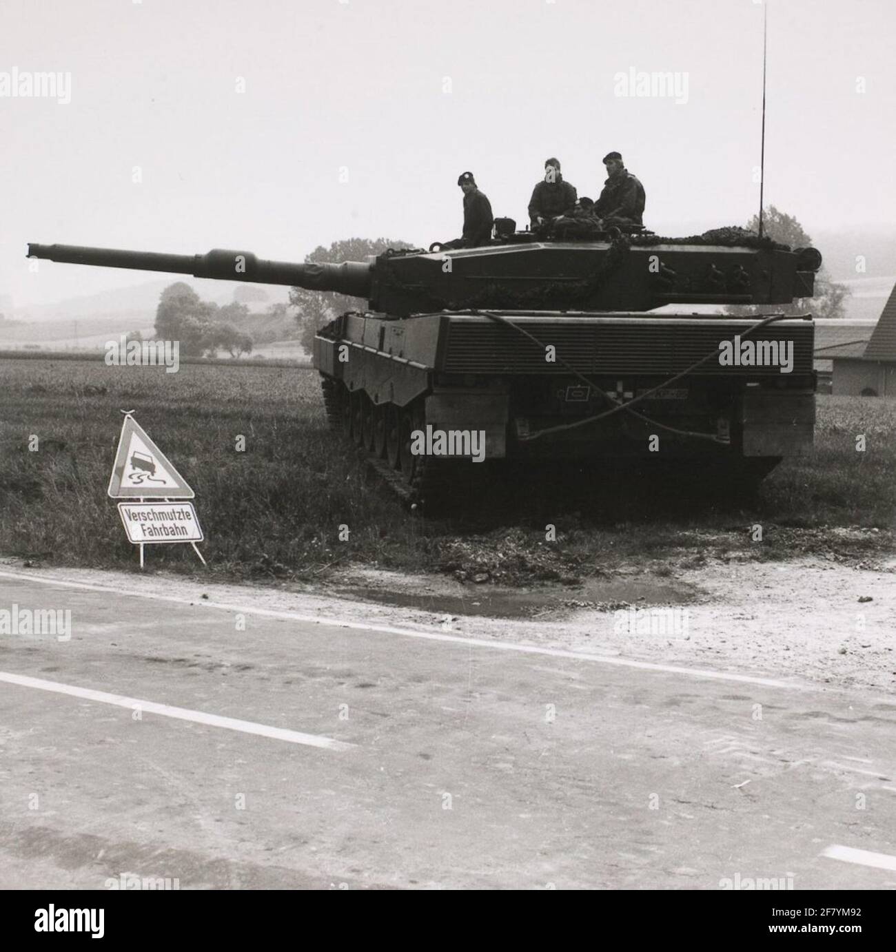 Rückseite eines holländischen Leopard 2 Panzers mit der Kuppel nach links gedreht. Das gekreuzte Abschleppseil am Heck ist gut zu erkennen. Das deutsche Warnschild im Vordergrund warnt vor verschmutzten Straßen (Schlamm e.d) und einer Rutschgefahr. Stockfoto