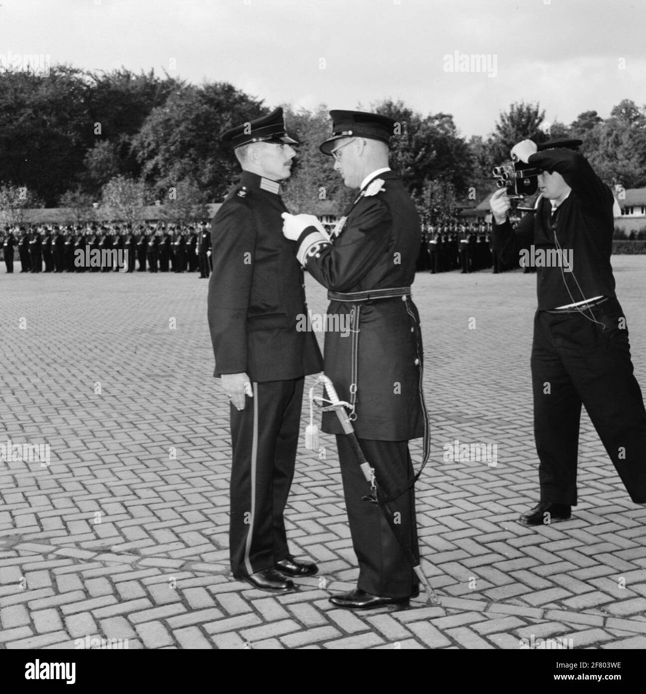 Beim Marines Corps, in der Van Braam Houckgeestkazerne (VBHKAZ) in Doorn, findet eine Medaillenübergabe statt. Der Kommandant der seetüchtigen Streitkräfte (BDZ) Vize-Admiral (VADM) A.H.J. Van der geschätzte Olivier kneift das Kreuz von Merge (kv) bei der Klasse Marinier der 1e (Marn. 1) C.L. Valentinstag. Rechts im Bild filmt der korporale Flugzeugfotograf (KplvgMRF) Jos van Haarlem (1933-2013), der später als erster in den neuen Special-Service-cineaEast-Dienst gehen sollte. Dieses Verdienstkreuz wird "wegen mutiger und politischer Maßnahmen in Niederländisch-Neuguinea" vergeben. Stockfoto