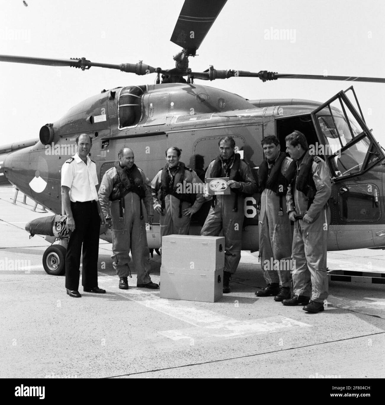 Lynx Hubschrauber mit Besatzung nach Ankunft des Nachfluges von RNAs Yeovilton. Der englische Flughafen war der Stuckplatz von 6,000 gelegentlichen Umschlägen, die mit dem 40. Jahrestag der Flugzeuggeschwader 860 und 65 Jahre MarineLiegkamp de Kooy in Verbindung gebracht wurden. Leutnant bei Seehandelsdienstleistungen wt.m. Unruhe hält die Erinnerungstafel dieses Fluges. Die Besatzung wurde von Commander Aircraft Quadron 860 Captain-Lieutenant auf See A. Veentjer empfangen. Stockfoto