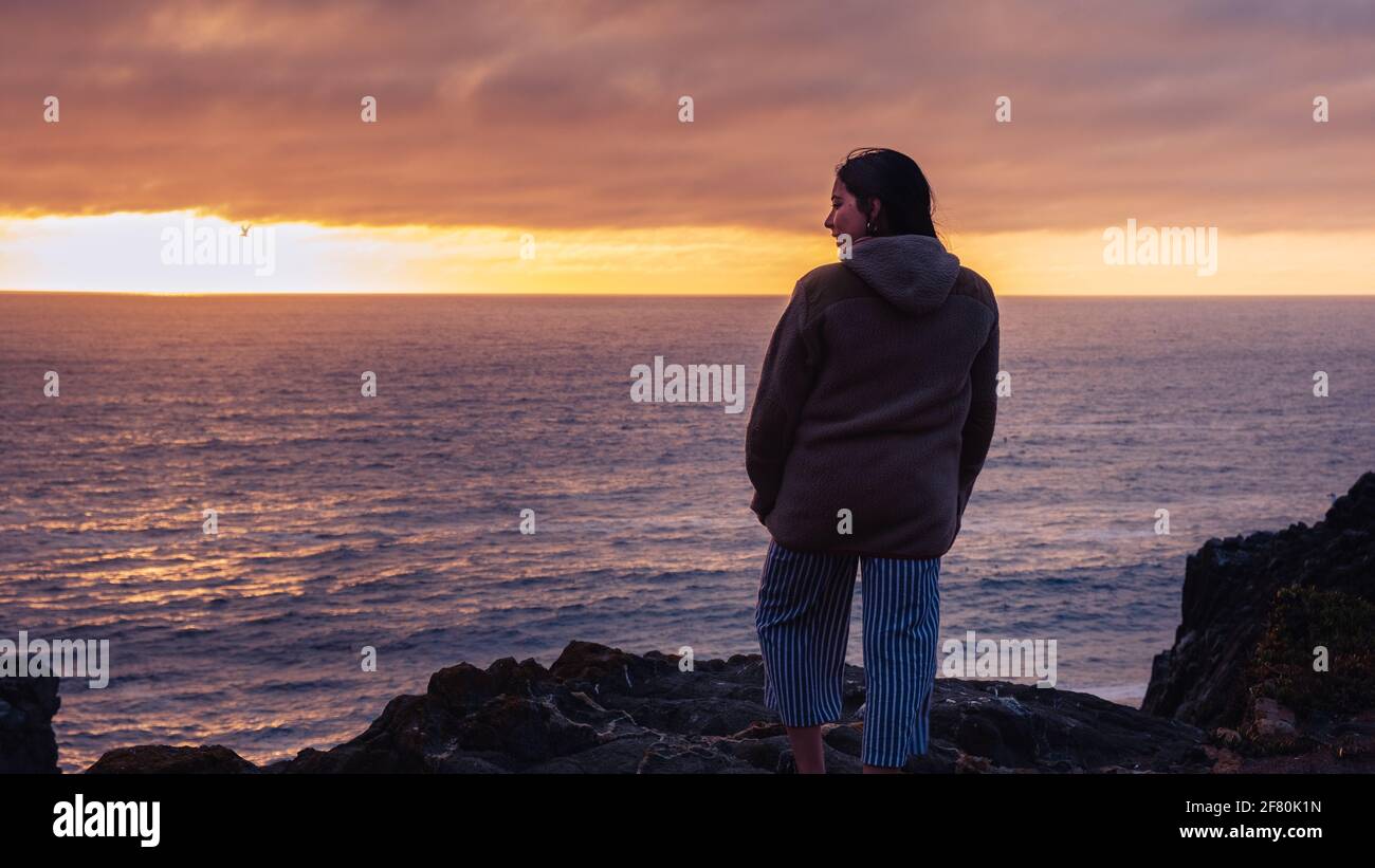 Frau, die einen Sonnenuntergang am Strand beobachtet Stockfoto