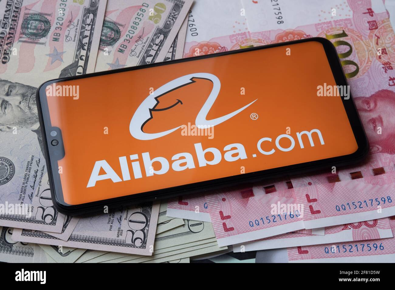 Alibaba-Logo auf dem Smartphone, das auf Geld platziert ist - US-Dollar und chinesischen Yuan gesehen. Unscharfer Hintergrund. Staffrod, Großbritannien, 10. April 2021. Stockfoto