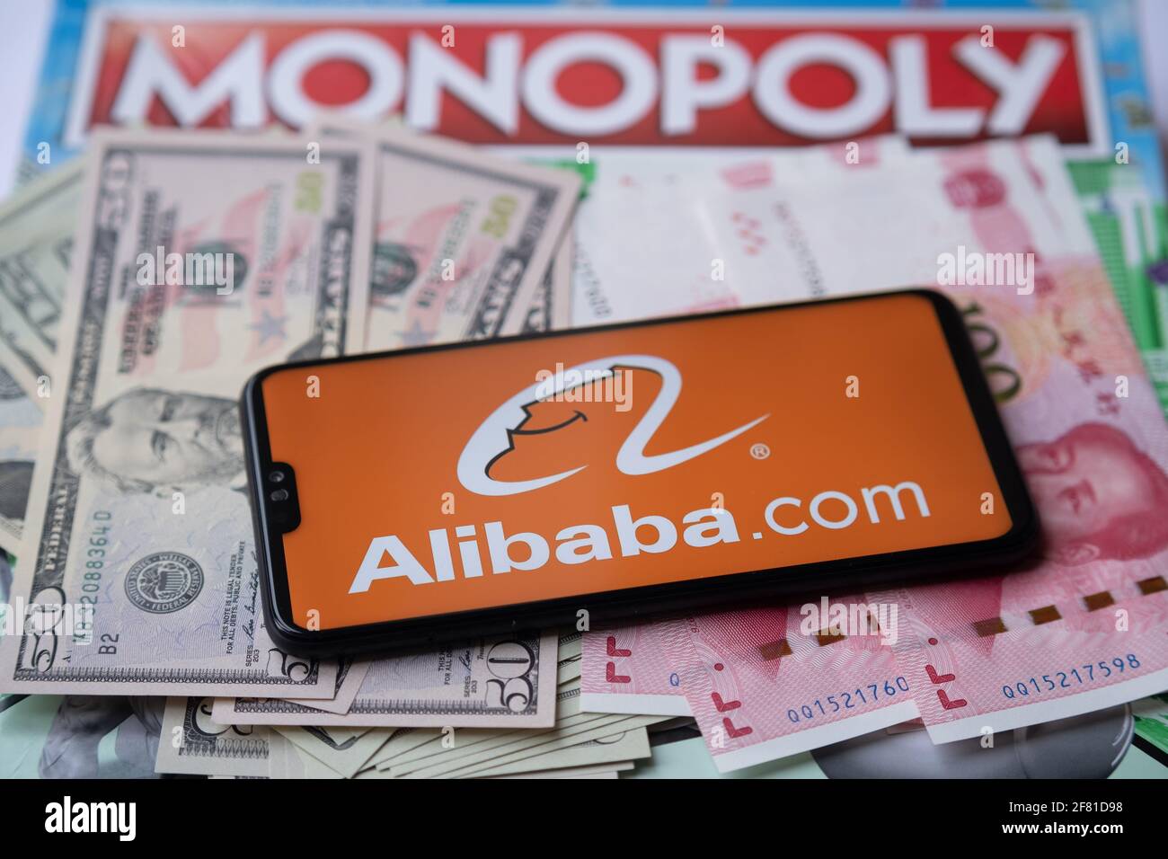 Alibaba-Logo auf dem Smartphone, das auf Geld platziert ist - US-Dollar und chinesischen Yuan, und Monopoly-Spiel auf dem verschwommenen Hintergrund. Konzept. Staffrod Stockfoto