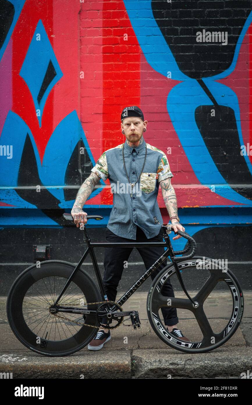 Junger Hipster Mann mit seinem Fahrrad vor Graffiti Wand Hintergrund. Stockfoto