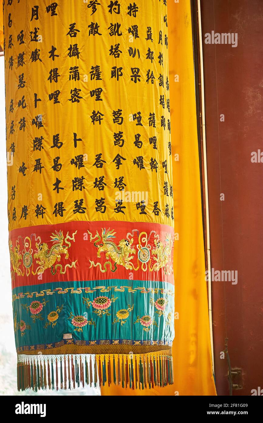Schwarze chinesische Schrift auf einem hängenden gelben Gebetsband mit genähten eleganten Drachen und Blumen, Lingyin Tempel, West Lake, Hangzhou, China Stockfoto