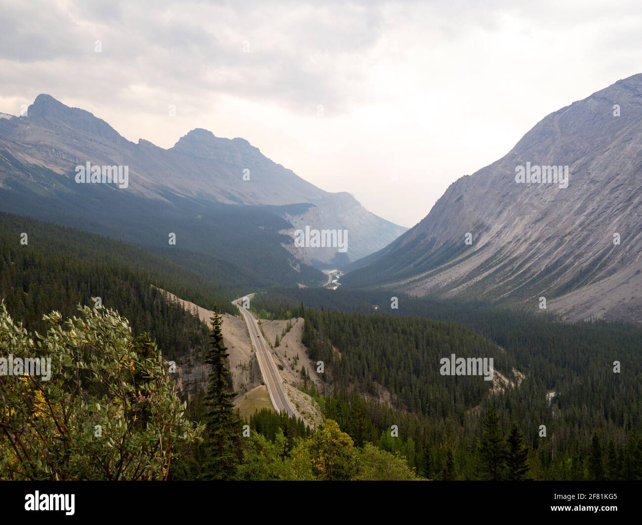 Blick auf ein Tal im Sommer mit einer Straße in Die Entfernung und die hohen Berge Stockfoto