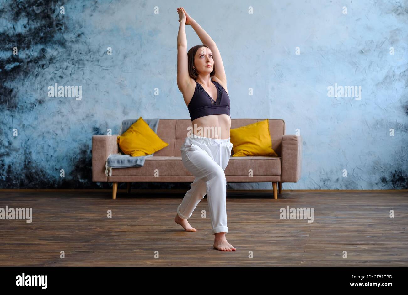 Frau in ihrem Wohnzimmer in Krieger-Yoga-Pose. Stockfoto