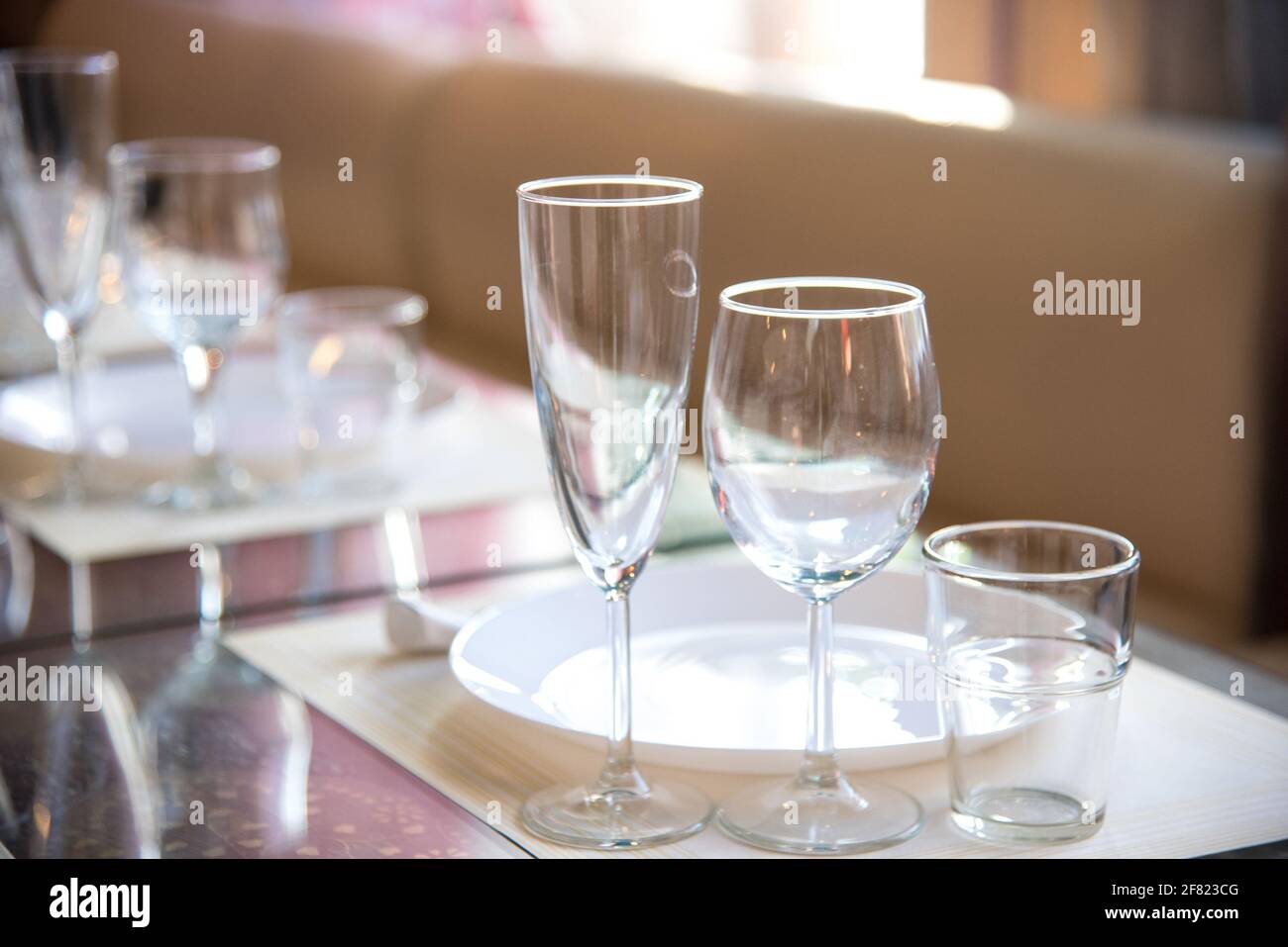 Im Restaurant wird ein Tisch mit Gläsern für Wein, Champagner und Cognac, Servietten und weißen Tellern für die Gäste serviert Stockfoto