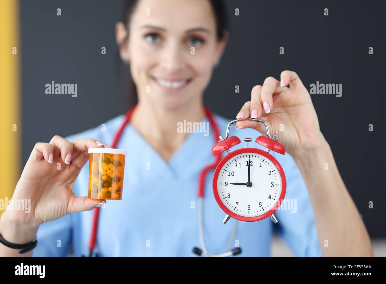 Lächelnder Arzt hält roten Wecker und Medikamente in sich Hand Stockfoto